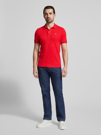 Männermodel trägt Regular Fit Poloshirt aus reiner Baumwolle von Lacoste in Optik: Unifarben mit Logo-Detail, Ganzkörperansicht von vorne.