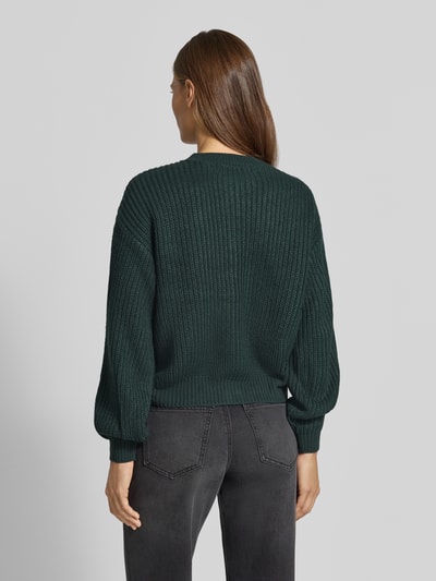 Frauenmodel trägt dunkelgrüne Loose Fit Strickjacke mit einreihiger Knopfleiste Modell 'LEA' von VERO MODA, gerippte Textur, Ganzkörperansicht Rückansicht.