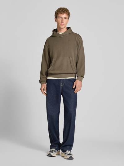 Männermodel trägt Regular Fit Hoodie aus reiner Baumwolle von G-Star RAW in Khaki mit Kängurutasche, kombiniert mit Jeans, Ganzkörperansicht von vorne.