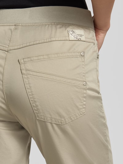 Kobieta nosi Caprihose mit elastischem Bund Modell 'Pamina' von Raphaela By Brax, bawełna z elastanem, krój regular fit, beż, detal tylnej kieszeni, zbliżenie na biodro