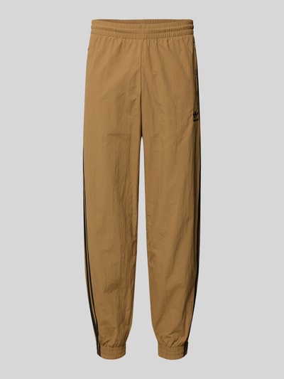 Produktfoto, Sweatpants mit elastischem Bund von adidas Originals w kolorze beżowym, luźny krój, elastyczny pas, kieszenie na zamek, naszywka z logo, długość nogawki wewnętrznej 77 cm dla rozmiaru M, tekstura gładka
