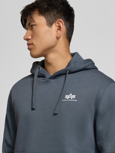 Männermodel trägt Hoodie mit Label-Details von Alpha Industries in Grau, Baumwoll-Mix, lockerer Schnitt, Nahaufnahme Oberkörper.