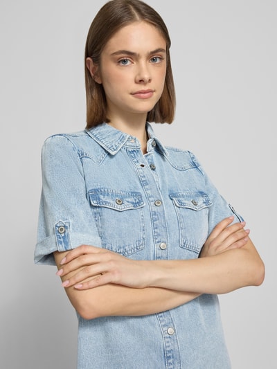Kobiece modelka nosi Körpernahes Jeanskleid aus Baumwoll-Viskose-Mix Modell 'LISA' od Only, jasnoniebieski denim, krótki rękaw, kieszenie na piersi, prosty kolor, krój slim fit, mini długość, widoczne przeszycia, zapięcie na guziki, całkowite zbliżenie górnej części ciała, Nahaufnahme Oberkörper.