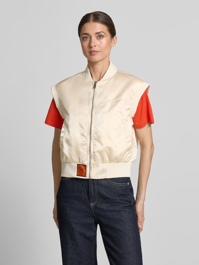 Frauenmodel trägt Weste mit Reißverschluss und Label-Detail von Original Bombers in Creme mit Stehkragen, Relaxed Fit, Eingrifftaschen, Ganzkörperansicht von vorne.