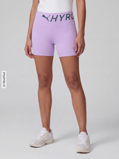 Frauenmodel trägt Skinny Fit Sportshorts mit Label-Print Modell 'PUMA x HYROX PWRMODE 4' von PUMA in Flieder, Ganzkörperansicht von vorne, Damen Sportshorts von PUMA Performance, KI-modifiziertes Bild.