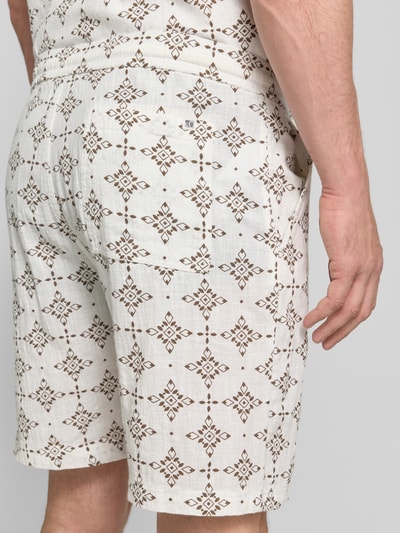 Männermodel trägt Relaxed Fit Stoffshorts aus einer Baumwolle von s.Oliver RED LABEL in beige mit braunem Muster, Ganzkörperansicht Rückansicht.