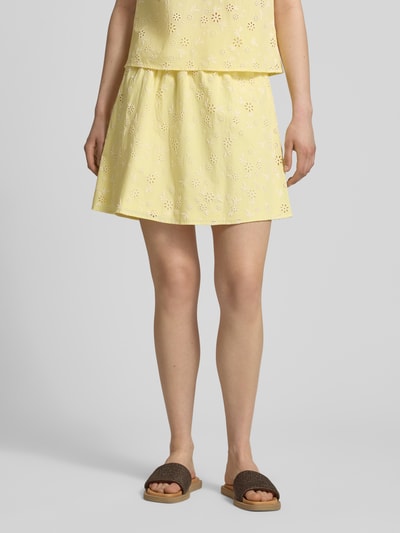 Frauenmodel trägt Regular Fit Mini-Rock aus reiner Baumwolle Modell 'BANNA' von Pieces in Gelb mit floralem Muster, Popeline-Textur, elastischer Bund, Ganzkörperansicht von vorne.