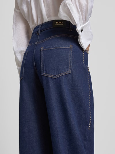 Frauenmodel trägt Barrel Fit Jeans aus reiner Baumwolle mit Strasssteinbesatz von Liu Jo, dunkles Blau, 5-Pocket-Design, Ganzkörperansicht Rückansicht. Kontext: Damen Jeans von Liu Jo White, Barrel Fit, Strasssteinbesatz, verkürzte Passform, Knopf- und Reißverschluss, Bundweite 39 cm, Innenbeinlänge 70 cm.