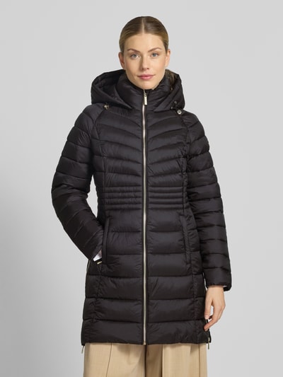 Modelka kobieca nosi czarny Steppmantel mit Reißverschlusstaschen und Kapuze von MICHAEL Michael Kors, prosty krój, kaptur ze ściągaczem, zamek błyskawiczny, boczne kieszenie na zamek, boczne zamki u dołu, długość tyłu w rozmiarze S: 87 cm, szerokość ramion w rozmiarze S: 45 cm, szerokość klatki piersiowej w rozmiarze S: 52 cm, długość rękawa w rozmiarze S: 59 cm, matowa tekstura, widok całej sylwetki z przodu