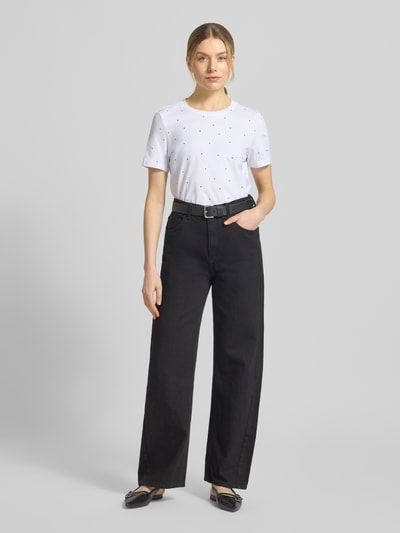 Modelka nosi Shaped Fit T-Shirt aus reiner Baumwolle Modell 'PAULINA AOP' od Vero Moda, biała koszulka z krótkim rękawem, allover, bawełniany jersey, widok całej sylwetki z przodu.