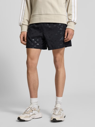 Mężczyznę model nosi Regular Fit Sport-Shorts mit Allover-Muster od adidas Training, czarny kolor, elastyczny pas, kieszenie boczne na zamek, całkowity widok z przodu.