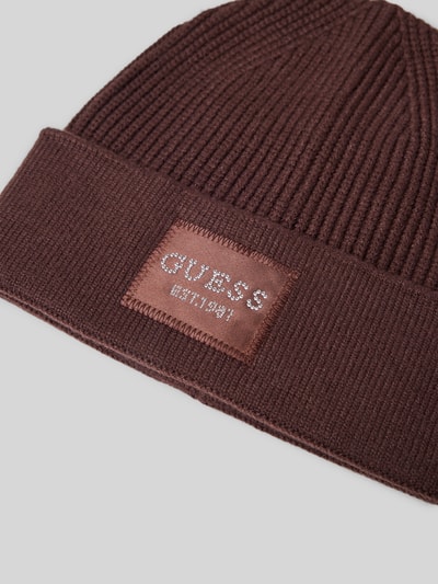 Produktfoto, Mütze aus Viskose-Mix in Strick-Optik von GUESS mit Logo-Patch und Strasssteinbesatz in Braun auf hellem Hintergrund.
