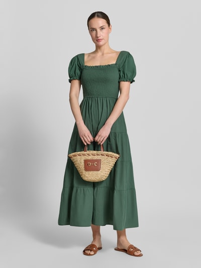 Frauenmodel trägt grüne Kleid und hält Handtasche mit Schulterriemen Modell 'CIES' von Mango, Naturtöne, Hauptfach, Tragehenkel, Ganzkörperansicht von vorne.