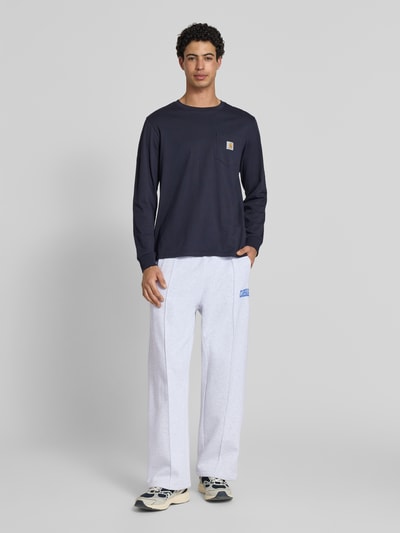 Männermodel trägt Sweatpants mit elastischem Bund und Label-Print von Carhartt Work In Progress aus Reine Baumwolle in Grau, Wide Leg, Längsnähte; Ganzkörperansicht von vorne.