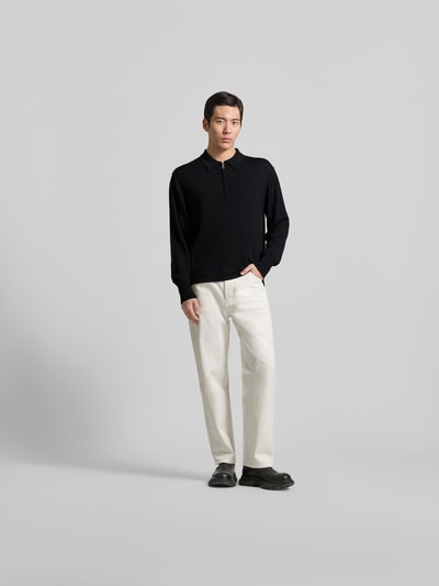 Männermodel trägt Pullover aus reiner Lanawolle von Officine Générale in Schwarz, Regular Fit, Polo-Kragen, weiße Hose, Ganzkörperansicht von vorne.