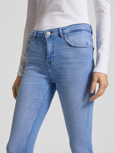 Kobiece modelka nosi Skinny Fit Jeans mit 5-Pocket-Design od Review, jasnoniebieski kolor, mieszanka bawełny z dodatkiem streczu, zapięcie na guzik i zamek, widoczna tekstura denimu, zbliżenie na okolice bioder, nahaufnahme okolic bioder.