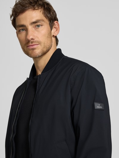 Männermodel trägt Bomberjacke mit Reißverschluss und Eingrifftaschen von JACK & JONES premium, krój regular fit, stójka, zamek błyskawiczny, wpuszczane kieszenie, długość tyłu w rozmiarze M: 66 cm, szerokość ramion w rozmiarze M: 42 cm, szerokość klatki piersiowej w rozmiarze M: 60 cm, długość rękawów w rozmiarze M: 68 cm, kolor granatowy, gładka powierzchnia, nahaufnahme górnej części ciała.