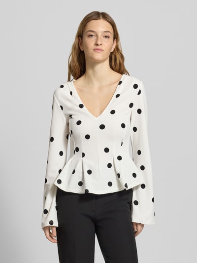 Kobiece model prezentuje bluzka z długim rękawem z dekoltem w serek Longsleeve mit V-Ausschnitt od Gina Tricot, mieszanka materiałów z dodatkiem streczu, taliowany krój, rozkloszowana dolna część, długość tyłu w rozmiarze S: 53 cm, białe tło z czarnymi kropkami, widok całej sylwetki z przodu.
