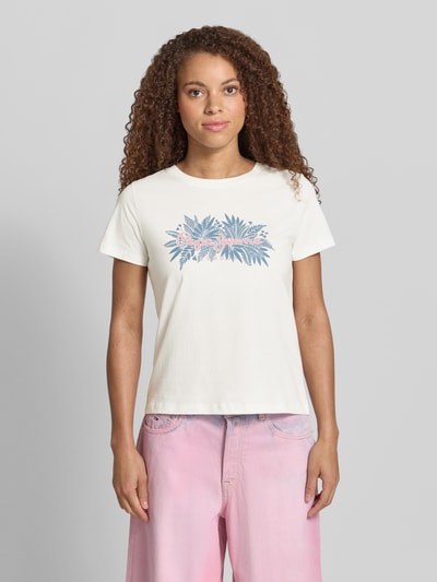 Frauenmodel trägt Boxy Fit Damen T-Shirt aus reiner Baumwolle Modell 'CRISTINA' von Pepe Jeans in Optik: Unifarben, Motiv-Print, Label-Print, Rundhals-Ausschnitt, Ärmelform: Kurzarm, Materialverarbeitung: Jersey, Material: Reine Baumwolle, Farbton Weiß, Blau und Rosa mit weicher Textur, Ganzkörperansicht von vorne.