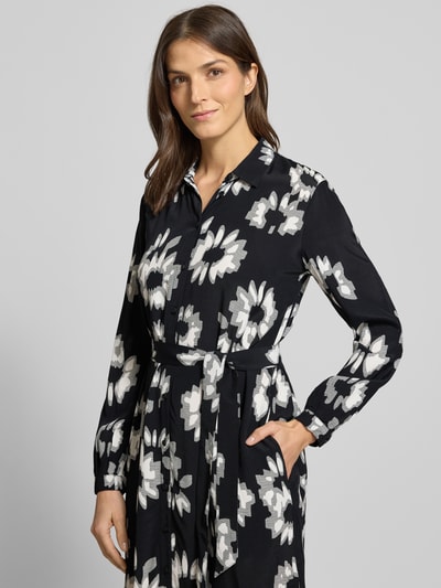Frauenmodel trägt Midikleid mit Bindegürtel von Esprit aus reiner Viskose mit floraler Allover-Print, gerader Schnitt, Umlegekragen, durchgehende Knopfleiste, Bindegürtel, lange Ärmel, Rückenlänge 118 cm, Brustweite 51 cm, Ärmellänge 64 cm, Schwarz-Weiß-Muster, Nahaufnahme Oberkörper.