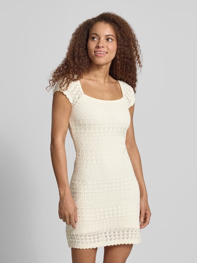 Frauenmodel trägt Strickkleid mit Strukturmuster und Wellensaum von REVIEW in Creme, gerader Schnitt, reine Baumwolle, Minikleid, Ganzkörperansicht von vorne.