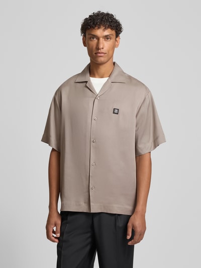 Männermodel trägt Relaxed Fit Freizeithemd aus reinem Lyocell Modell 'ESPINO' von HUGO in Uni-Taupe, Kurzarm, Logo-Patch, Ganzkörperansicht von vorne.