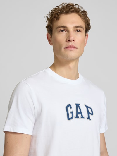 Männermodel trägt T-Shirt mit Logo-Patch und Rundhalsausschnitt von GAP, weiße Baumwolle, Straight Fit, Nahaufnahme Oberkörper.