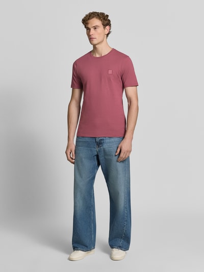 Mężczyznamodel nosi Regular Fit T-Shirt aus reiner Baumwolle Modell 'TALES' von BOSS Orange w kolorze ceglastym, granatowe dżinsy, jasne buty, neutralne tło, Ganzkörperansicht von vorne.