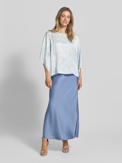 Modelka nosi Loose Fit Poncho-Bluse mit Allover-Muster od s.Oliver BLACK LABEL, efekt: wzór na całej powierzchni, krój loose fit, dekolt w łódkę, rękawy nietoperzowe, wykończenie materiału: tkanina, materiał: czysta wiskoza, jasnoniebieskie i kremowe barwy, gładka faktura, widok całej sylwetki z przodu.