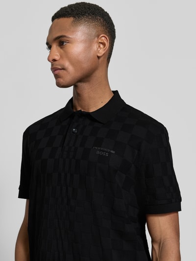 Männermodel trägt Poloshirt aus reiner Baumwolle Modell 'JACQ' von BOSS Green x Porsche, schwarz, Strukturmuster, Nahaufnahme Oberkörper.