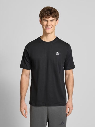 Männermodel trägt schwarzes T-Shirt mit Label-Stitching von adidas Originals aus reiner Baumwolle, Regular Fit, Nahaufnahme Oberkörper.