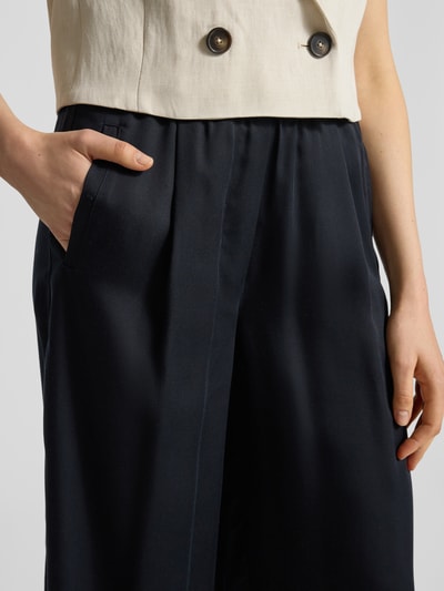Frauenmodel trägt Wide Leg Stoffhose mit elastischem Bund von Lanius, reine Lyocell, schwarze Farbe, Eingrifftaschen, Nahaufnahme Oberkörper.