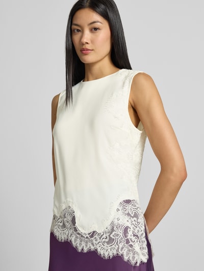 Frauenmodel trägt Top mit Spitzenbesatz Modell 'PELLA' von YAS, cremefarben, asymmetrische Form, Material-Mix, Nahaufnahme Oberkörper.