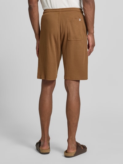 Männermodel trägt Relaxed Fit Sweatshorts aus Baumwoll-Mix von s.Oliver RED LABEL in Braun, strukturierte Piqué-Optik, aufgesetzte Gesäßtasche, Ganzkörperansicht Rückansicht.