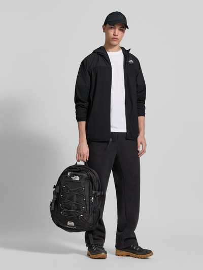 Męski model nosi Jacke mit Logo und Reißverschluss od The North Face, czarny materiał z dodatkiem stretchu, krój regular fit, logo, kaptur, zamek, długość tyłu w rozmiarze M: 63 cm, szerokość ramion w rozmiarze M: 48 cm, szerokość klatki piersiowej w rozmiarze M: 33 cm, długość rękawa w rozmiarze M: 65 cm, pełny widok z przodu