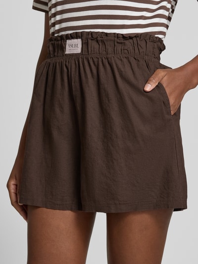 Frauenmodel trägt Regular Fit Stoffshorts aus Leinen-Baumwoll-Mix Modell 'MILLIE' von VILLA SOPHIE, braun, mit Allover-Muster, Label-Patch, elastischem Bund und seitlichen Eingrifftaschen, Material mit weicher Textur, Nahaufnahme Oberkörper.