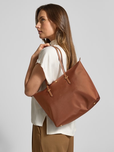 Frauenmodel trägt Tote Bag mit Label-Applikation Modell 'KEATON' von Lauren Ralph Lauren, braun, Tragehenkel, Hauptfach mit Reißverschluss, Ganzkörperansicht von vorne, Kontext: Damen Tote Bag, Breite 37 cm, Länge 28 cm, Tiefe 13 cm, Länge Schulterriemen 54 cm.