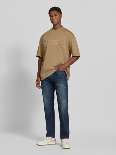 Männermodel trägt Straight Fit Jeans aus Baumwoll-Mix Modell 'C-Ogden' von BOSS in Dunkelblau, kombiniert mit beigem T-Shirt, Ganzkörperansicht von vorne, Herren Straight Fit Jeans von BOSS.
