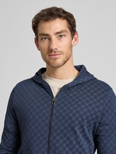 Männermodel trägt Sweatjacke mit Logo-Muster und Kapuze von JOOP! Collection aus Reine Baumwolle, Regular-Fit, Nahaufnahme Oberkörper.