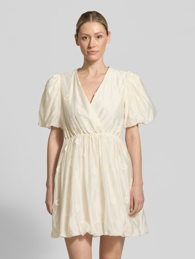 Frauenmodel trägt Minikleid mit V-Ausschnitt Modell 'CHAYA' von SUNCOO PARIS aus Lyocell-Mix, taillierte Passform, Puffärmel, Wickel-Optik, Rückenlänge 89 cm, Brustweite 42 cm, Ärmellänge 21 cm, cremefarben mit zarter Textur, Ganzkörperansicht von vorne.