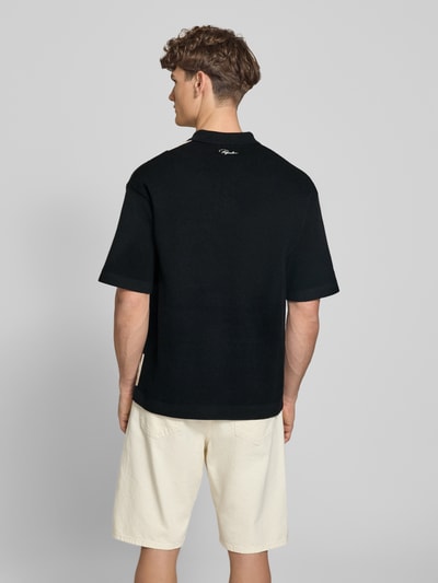 Mężczyzna model nosi czarną koszulkę polo Relaxed Fit Poloshirt in Strick-Optik model 'Tellero' od Pegador z bawełny, krótkie rękawy, kołnierzyk polo, długość tyłu w rozmiarze M: 73 cm, imitacja dzianiny, widok całej sylwetki z tyłu.