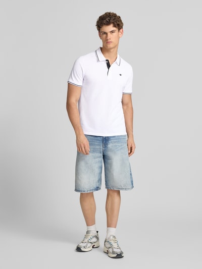 Männermodel trägt Slim Fit Poloshirt mit Label-Stitching von CHAMPION in Weiß, reine Baumwolle, Knopfleiste, Ganzkörperansicht von vorne.