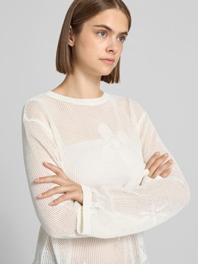 Kobieta nosi sweter z dzianiny z bawełny OH APRIL Strickpullover mit Rundhalsausschnitt Modell 'Ronja', krój regular fit, okrągły dekolt, wyhaftowane logo, kolor kremowy, gładka faktura, zbliżenie na górną część ciała z przodu.