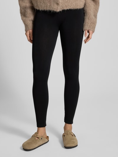 Frauenmodel trägt Leggings aus Viskose-Mix im nahtlosen Design Modell 'BAMBOO' von MAGIC Bodyfashion, schwarz, elastischer Bund, unifarben, feuchtigkeitsabsorbierend, enganliegend, Ganzkörperansicht von vorne.