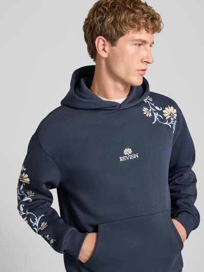 Männermodel trägt Relaxed Fit Hoodie mit Känguru-Tasche von REVIEW, florale Stickerei, navy, Baumwoll-Mix, Nahaufnahme Oberkörper.