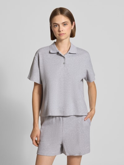 Frauenmodel trägt Relaxed Fit Poloshirt mit Strukturmuster Modell 'Noa' von OH APRIL in Hellgrau, kurze Ärmel, Knopfleiste, Nahaufnahme Oberkörper, Damen Poloshirt von OH APRIL, Rückenlänge bei Größe S: 55 cm.