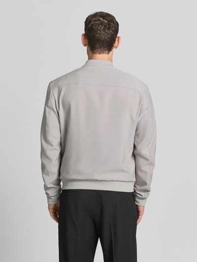 Männermodel trägt Blouson mit seitlichen Eingrifftaschen von MCNEAL in Hellgrau, elastische Abschlüsse, Material-Mix, Ganzkörperansicht Rückansicht.