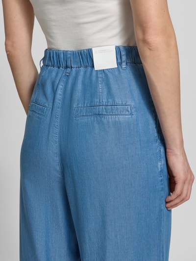 Frauenmodel trägt Wide Fit Jeans aus reinem Lyocell mit Bundfalten von Marc Cain, Paspeltaschen, teilelastischer Bund, Nahaufnahme Rückansicht. Damen Jeans mit Eingrifftaschen, Knopf- und Reißverschluss, Bundweite 36 cm, Innenbeinlänge 83 cm, glatte blaue Textur.