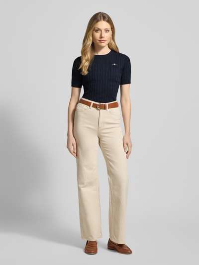 Frauenmodel trägt Strickshirt mit Zopfmuster und Label-Stitching von Gant in Dunkelblau, kombiniert mit heller Hose, Ganzkörperansicht von vorne.