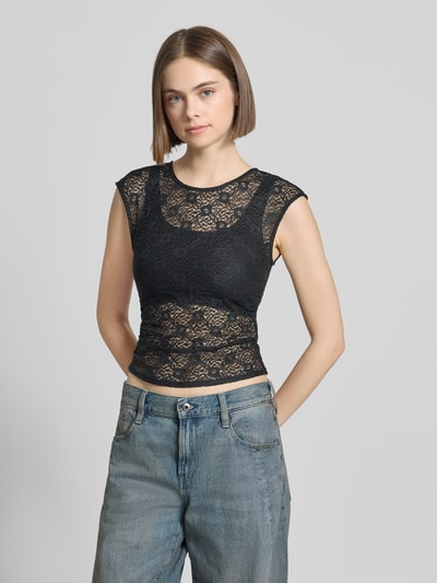 Frauenmodel trägt T-Shirt aus Spitze mit Raffung an der Seitennaht von REVIEW in Schwarz, Elastischer-Material-Mix, Körpernahe Passform, Rundhalsausschnitt, Rückenlänge bei Größe S: 45 cm, Ganzkörperansicht von vorne.
